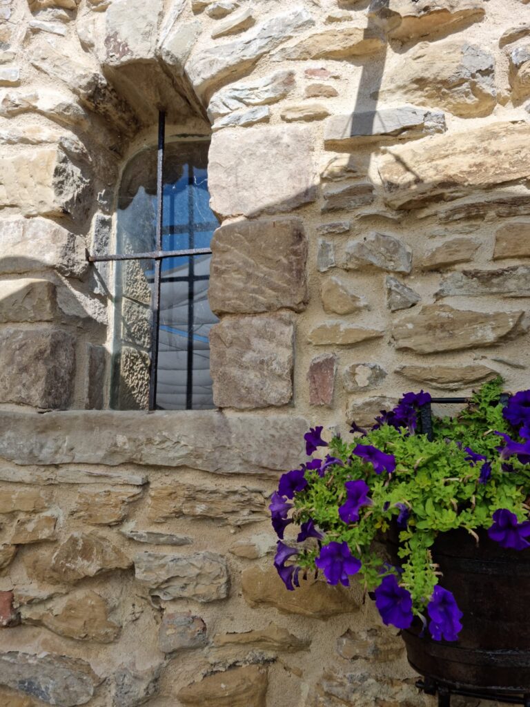 Dettaglio esterno della Torre della Soara: finestra con cornice in pietra serena, fiori viola nel vaso e facciata in pietra a vista, simbolo dell'accoglienza rurale umbra.