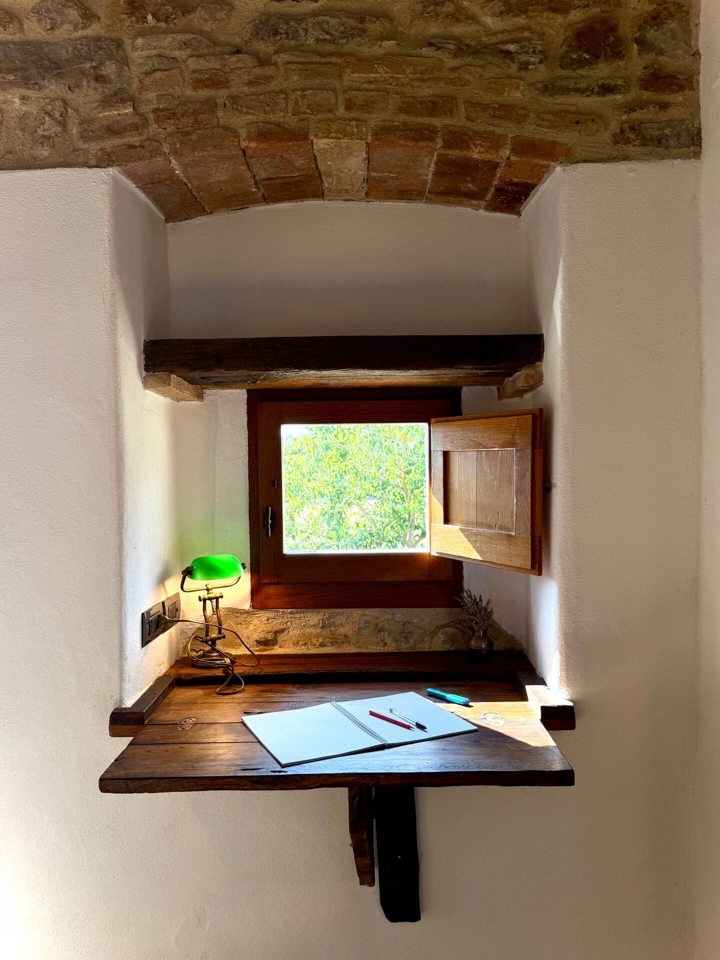 Angolo studio ricavato in una nicchia alla Torre della Soara: scrivania a ribalta in legno antico sotto una piccola finestra affacciata sul verde, con lampada ministeriale verde e soffitto a volta in mattoni. Angolo studio ricavato in una nicchia alla Torre della Soara: scrivania a ribalta in legno antico sotto una piccola finestra affacciata sul verde, con lampada ministeriale verde e soffitto a volta in mattoni.