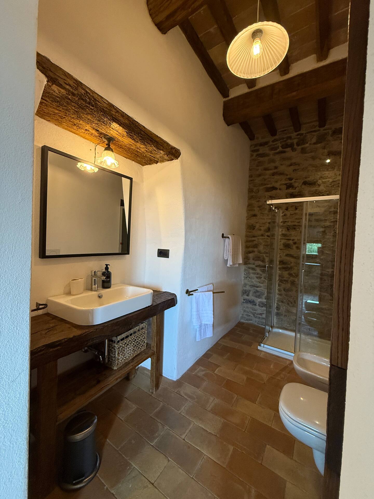 Ampio bagno della Torre della Soara: lavabo moderno su mensola in legno massiccio, parete in pietra antica a vista nella zona doccia e sanitari, soffitto con travi in legno e pavimento in cotto. Ampio bagno della Torre della Soara: lavabo moderno su mensola in legno massiccio, parete in pietra antica a vista nella zona doccia e sanitari, soffitto con travi in legno e pavimento in cotto.