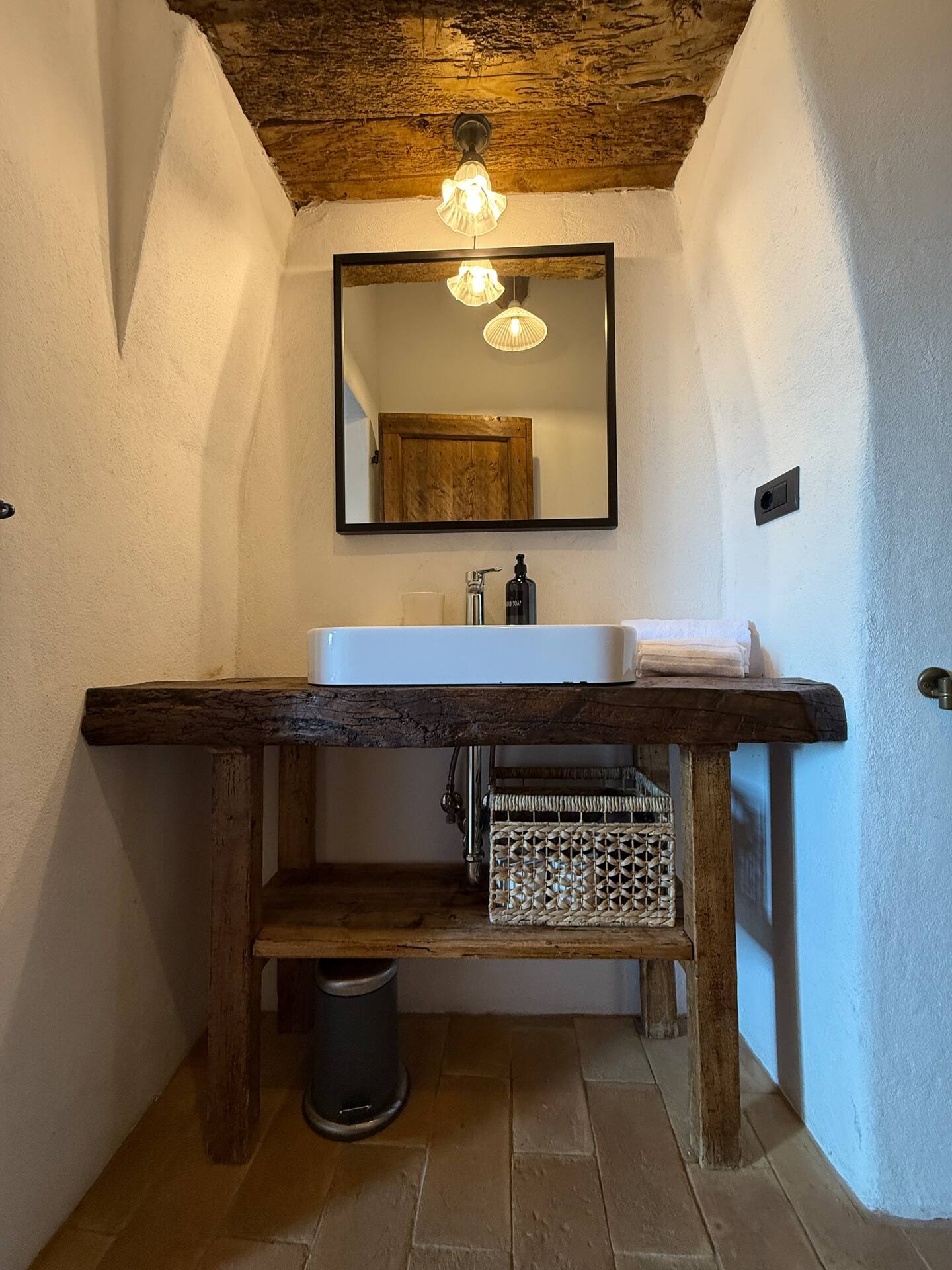 Dettaglio zona lavabo alla Torre della Soara: lavabo moderno a ciotola su mobile in legno massiccio grezzo, incassato in una nicchia di pareti bianche con architrave in legno scuro e specchio dal design minimale. Dettaglio zona lavabo alla Torre della Soara: lavabo moderno a ciotola su mobile in legno massiccio grezzo, incassato in una nicchia di pareti bianche con architrave in legno scuro e specchio dal design minimale.