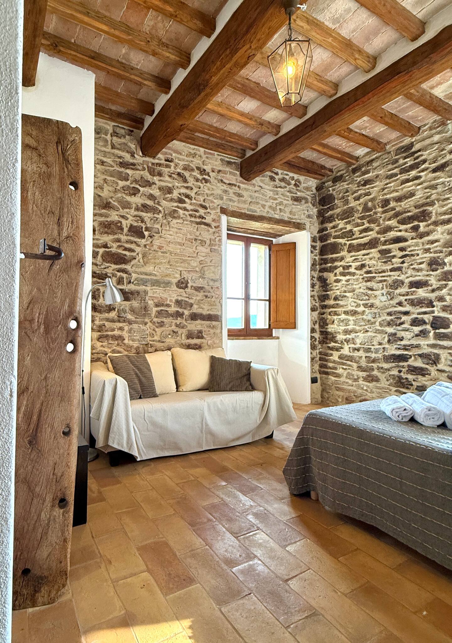 Angolo relax nella suite della Torre della Soara: divano chiaro con cuscini a contrasto posizionato davanti a una finestra con scuri in legno, circondato da pareti in pietra a vista e illuminato da una lampada di design e una lanterna a soffitto. Angolo relax nella suite della Torre della Soara: divano chiaro con cuscini a contrasto posizionato davanti a una finestra con scuri in legno, circondato da pareti in pietra a vista e illuminato da una lampada di design e una lanterna a soffitto.