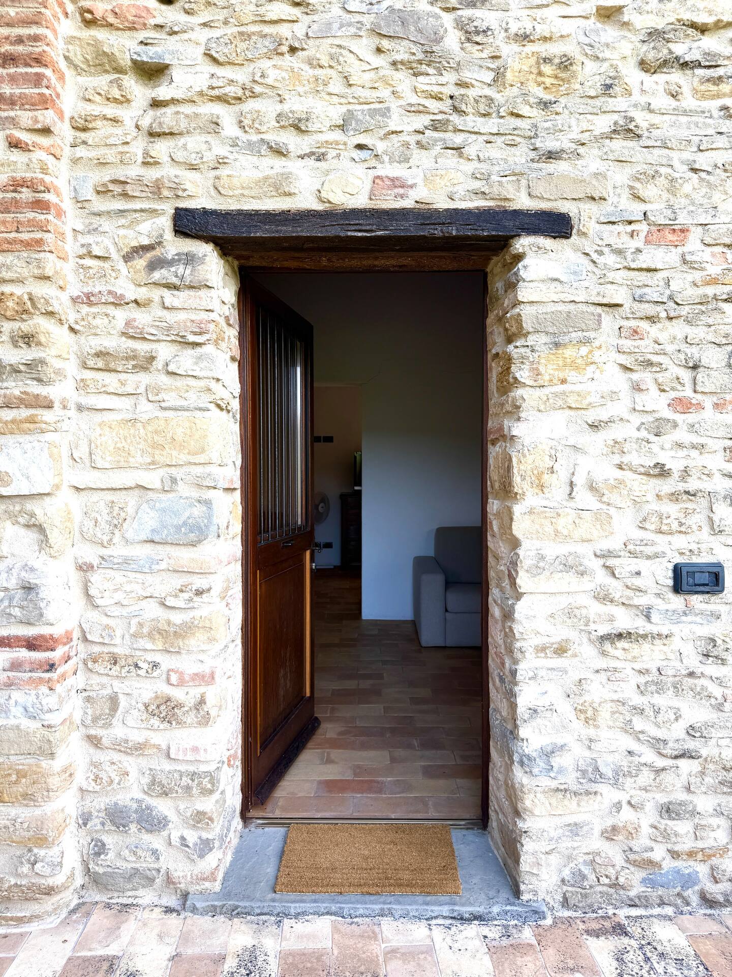 Ingresso dell'Appartamento Nido alla Torre della Soara: antica porta in legno aperta su pareti in pietra a vista, architrave in legno scuro e pavimento in cotto che conduce alla zona living. Ingresso dell'Appartamento Nido alla Torre della Soara: antica porta in legno aperta su pareti in pietra a vista, architrave in legno scuro e pavimento in cotto che conduce alla zona living.
