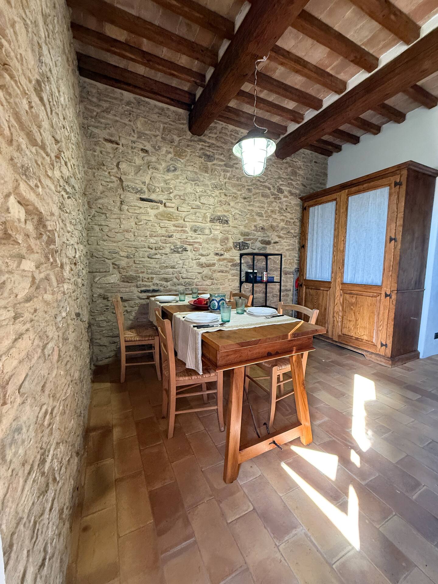 Sala da pranzo rustica alla Torre della Soara: tavolo in legno massello tra pareti in pietra originale, illuminato da una lampada a sospensione d'epoca, con cucina a scomparsa in armadio antico sullo sfondo. Sala da pranzo rustica alla Torre della Soara: tavolo in legno massello tra pareti in pietra originale, illuminato da una lampada a sospensione d'epoca, con cucina a scomparsa in armadio antico sullo sfondo.