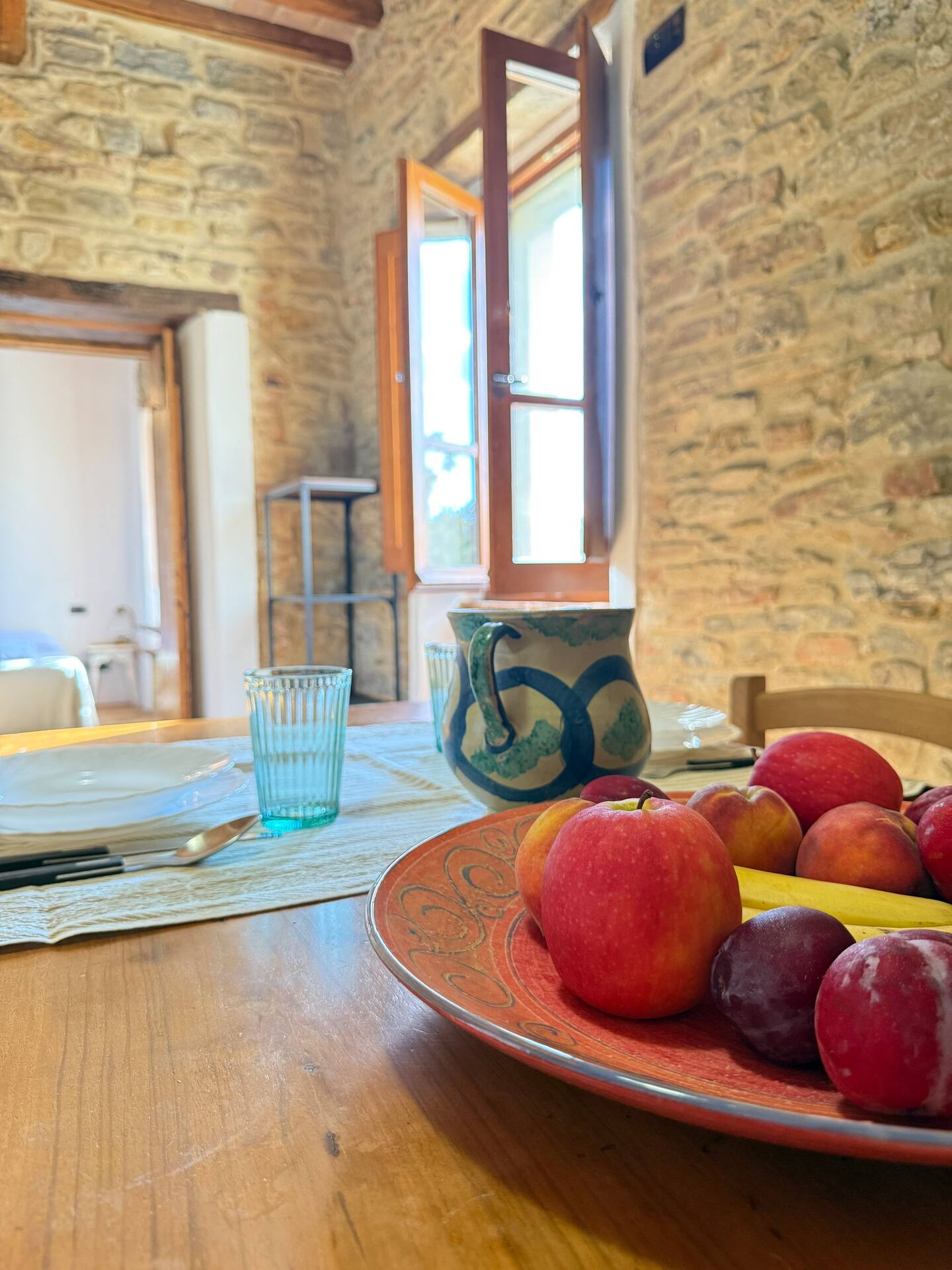 Dettaglio colazione alla Torre della Soara: vassoio di frutta fresca di stagione e brocca in ceramica artigianale su tavolo in legno, con vista sulle pareti in pietra e finestra aperta. Dettaglio colazione alla Torre della Soara: vassoio di frutta fresca di stagione e brocca in ceramica artigianale su tavolo in legno, con vista sulle pareti in pietra e finestra aperta.
