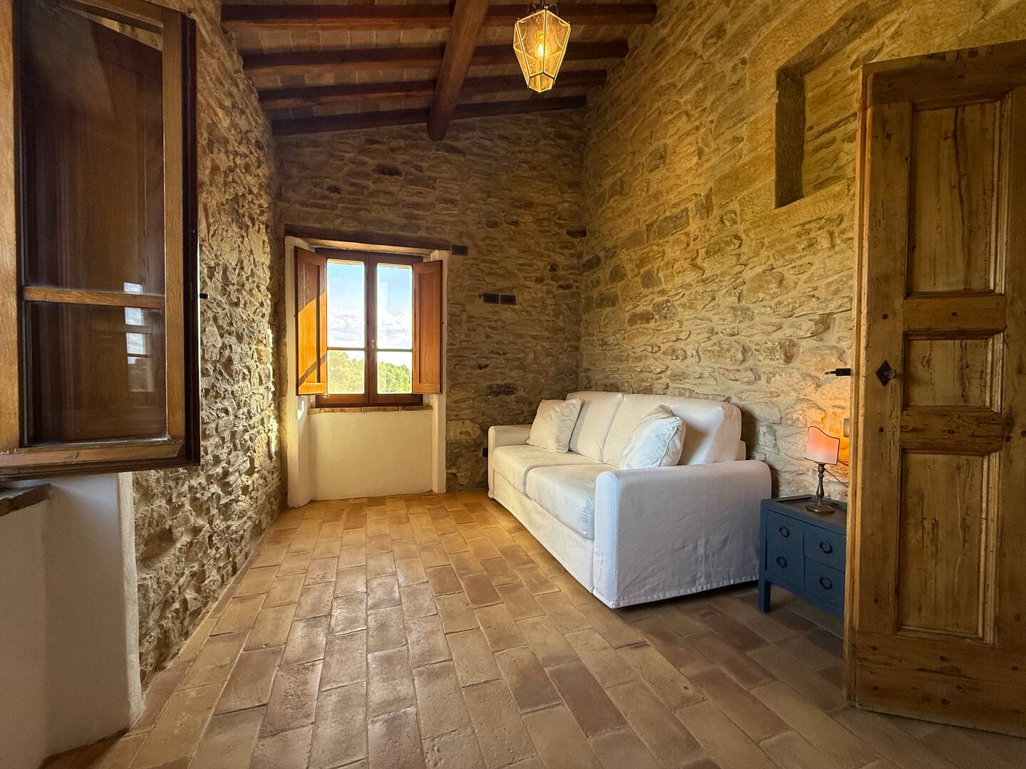 Area soggiorno e studio alla Torre della Soara: un accogliente divano bianco accostato a una parete in pietra antica, con un pavimento in cotto caldo e una finestra aperta che illumina la stanza con luce naturale. Area soggiorno e studio alla Torre della Soara: un accogliente divano bianco accostato a una parete in pietra antica, con un pavimento in cotto caldo e una finestra aperta che illumina la stanza con luce naturale.