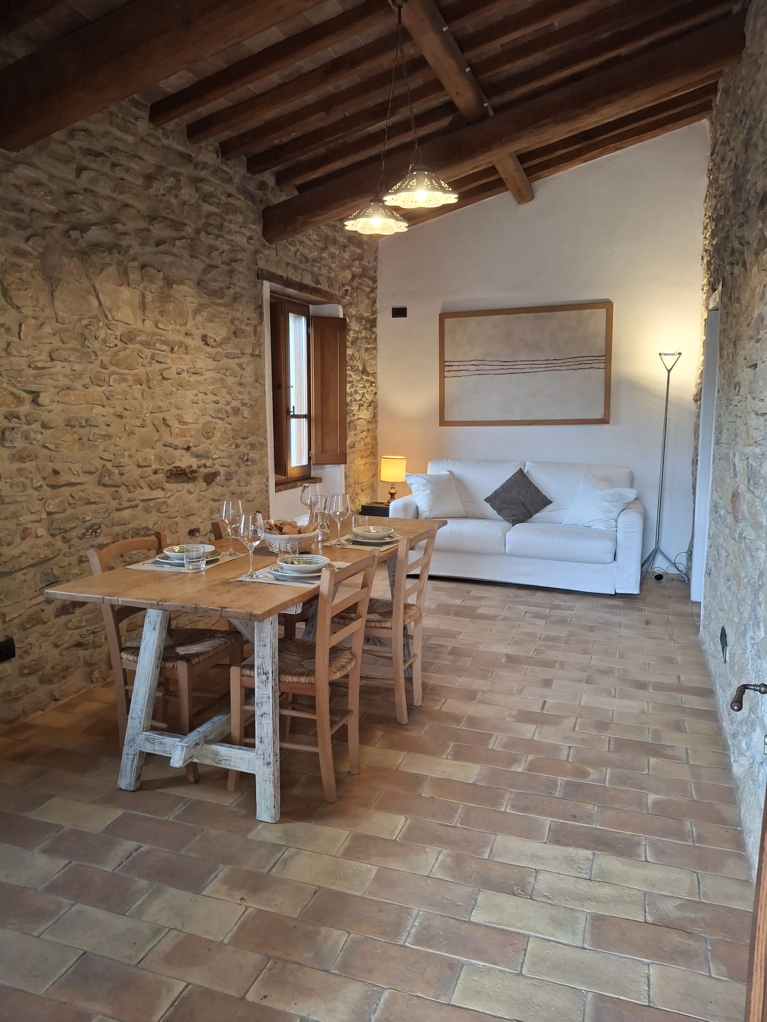 Soggiorno dell’appartamento Torre alla Torre della Soara, con tavolo da pranzo in legno apparecchiato, parete in pietra a vista, pavimento in cotto e zona relax con divano.