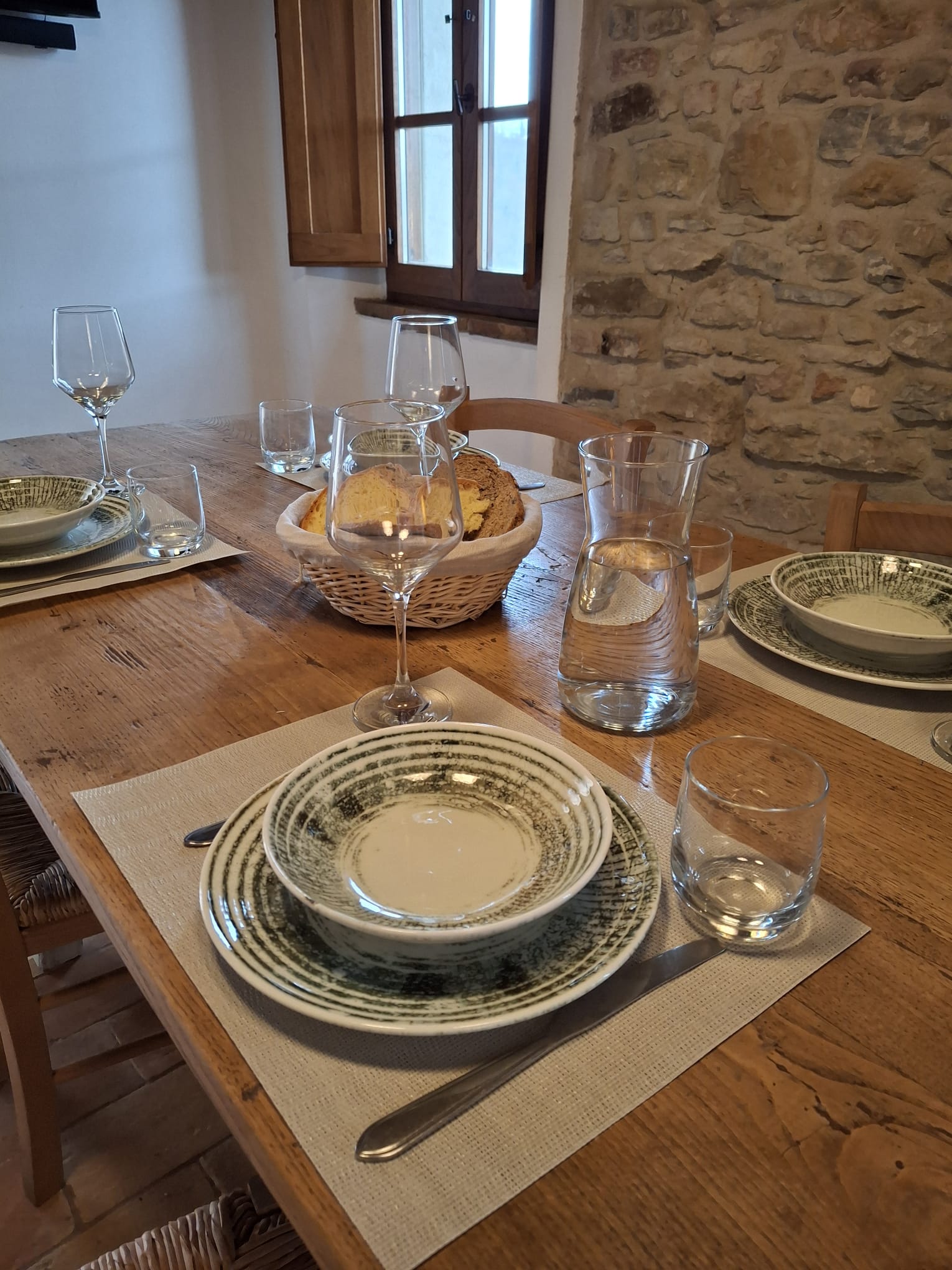 Tavola apparecchiata nell’appartamento Torre della Torre della Soara, con stoviglie in ceramica, bicchieri e dettagli in legno, accanto a una parete in pietra e a una finestra luminosa.